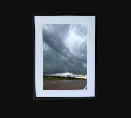Fine art print of large storm clouds building over a train and factory. Framed view