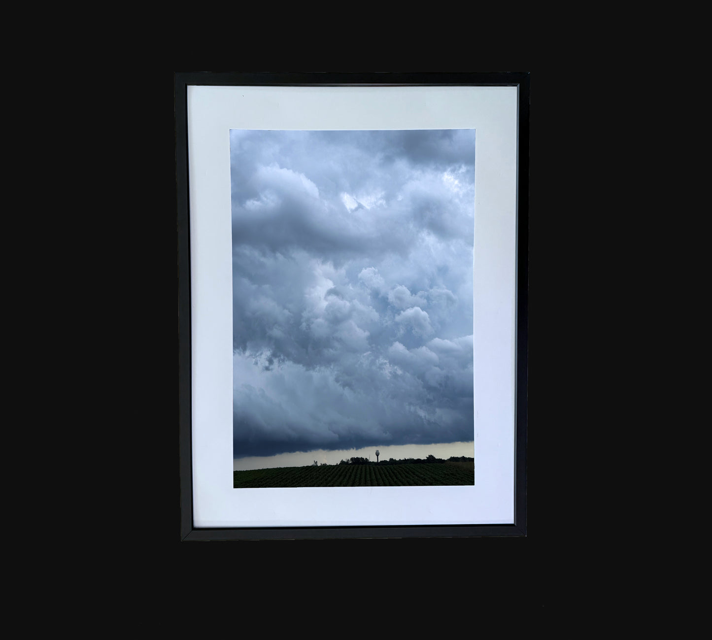 Fine art print of large storm clouds building over a rural town and corn field. Framed view