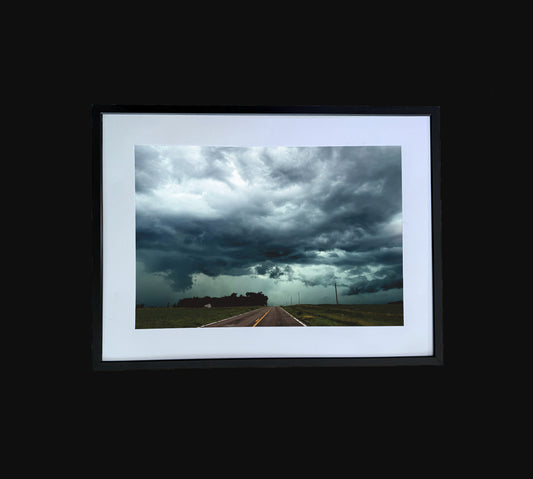 Fine art print of large storm clouds building over a rural road. Framed view