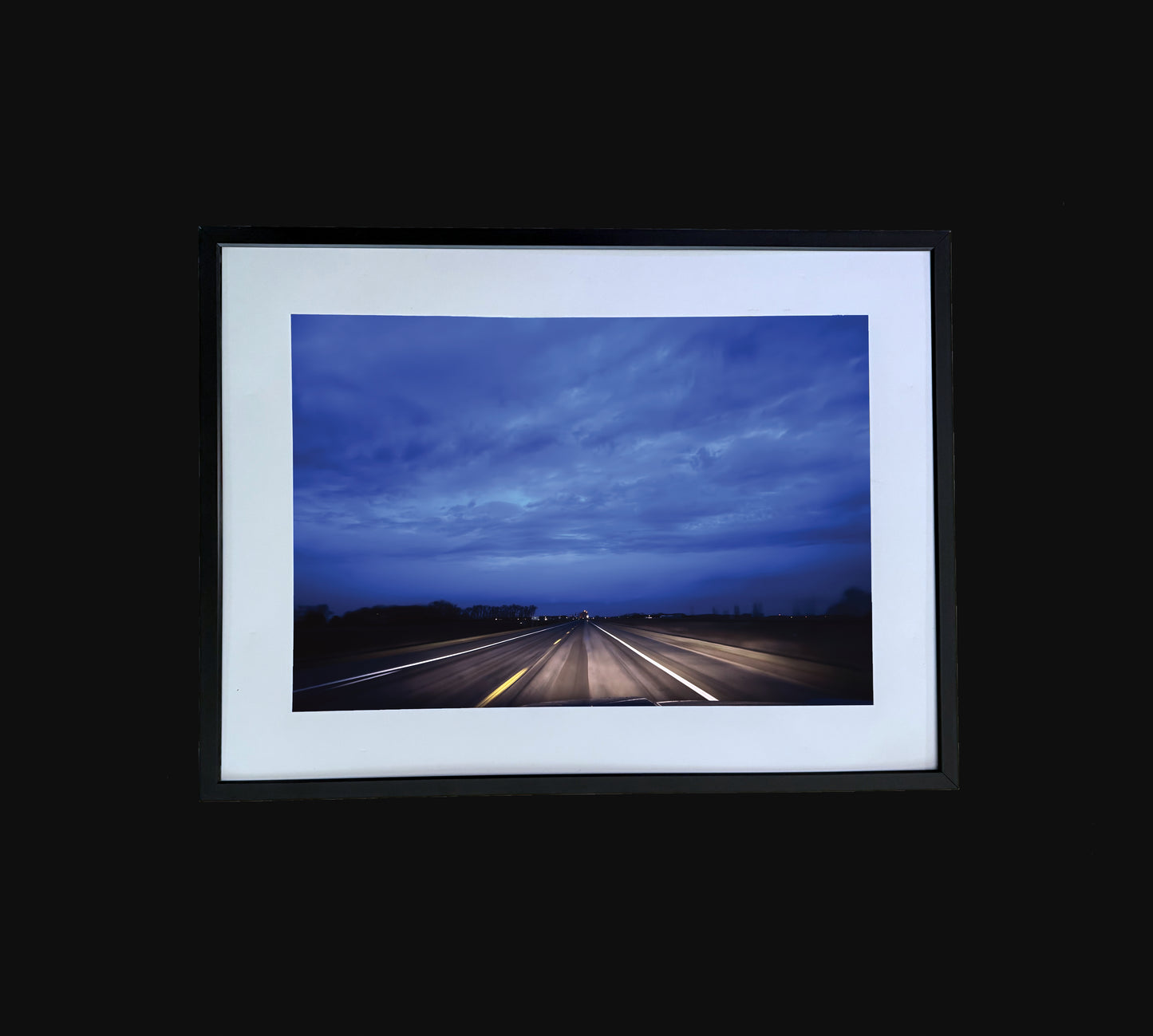 Fine art print of large clouds over road.  Framed view.