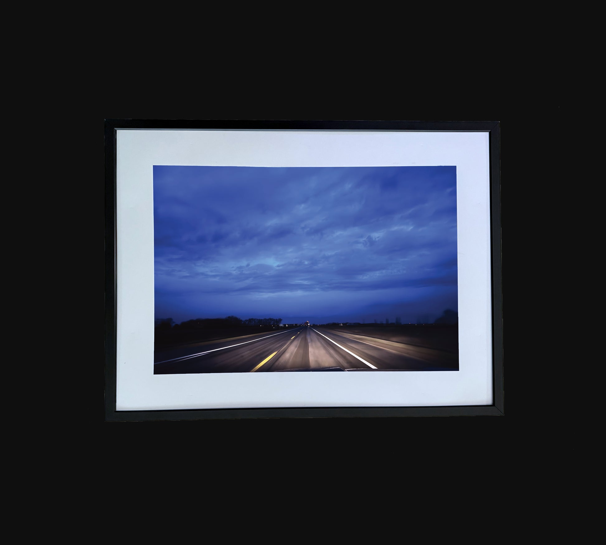 Fine art print of large clouds over road.  Framed view.