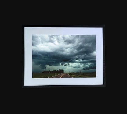 Fine art print of large storm clouds  building over a rural road.  Framed view