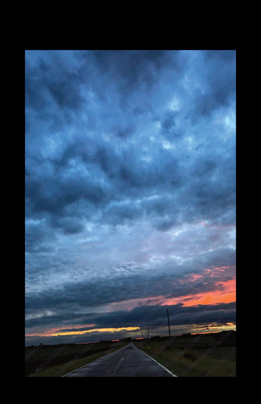 Fine art print of large clouds after a storm and sunset over rural road.  Print view